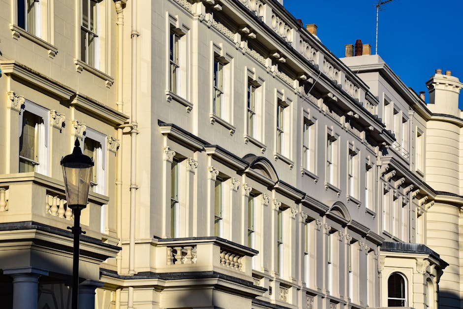 A close-up view of a historic cream-colored building with ornate architectural details, including decorative moldings and window frames. The building features multiple large, rectangular windows with