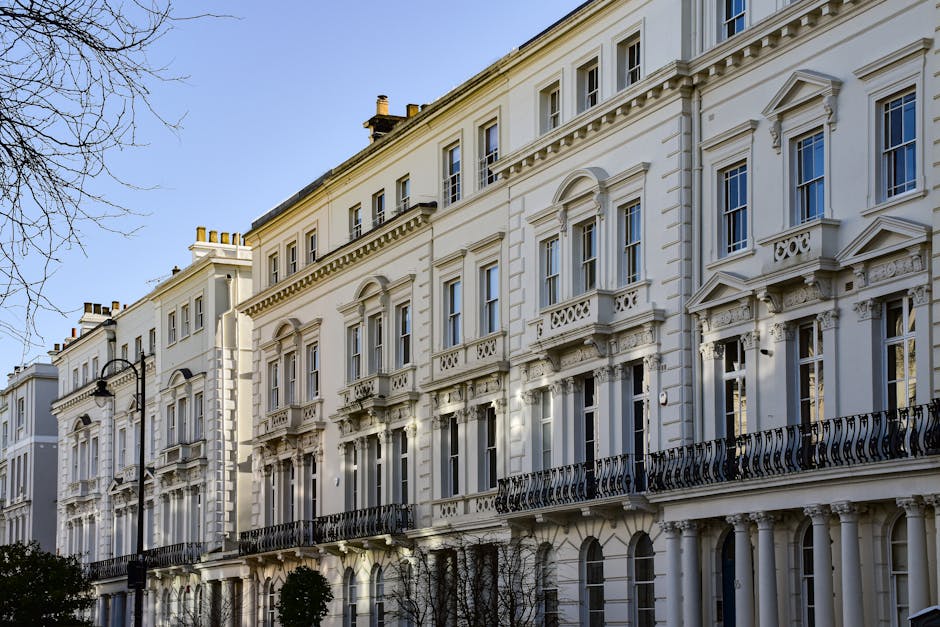 A close-up view of a historic cream-colored building with ornate architectural details, including decorative moldings and window frames. The building features multiple large, rectangular windows with